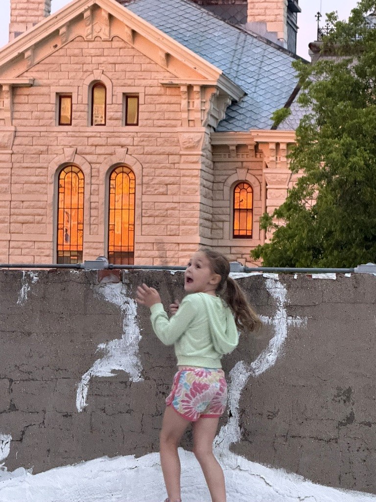A child on a balcony with the Hood County Courthouse behind her